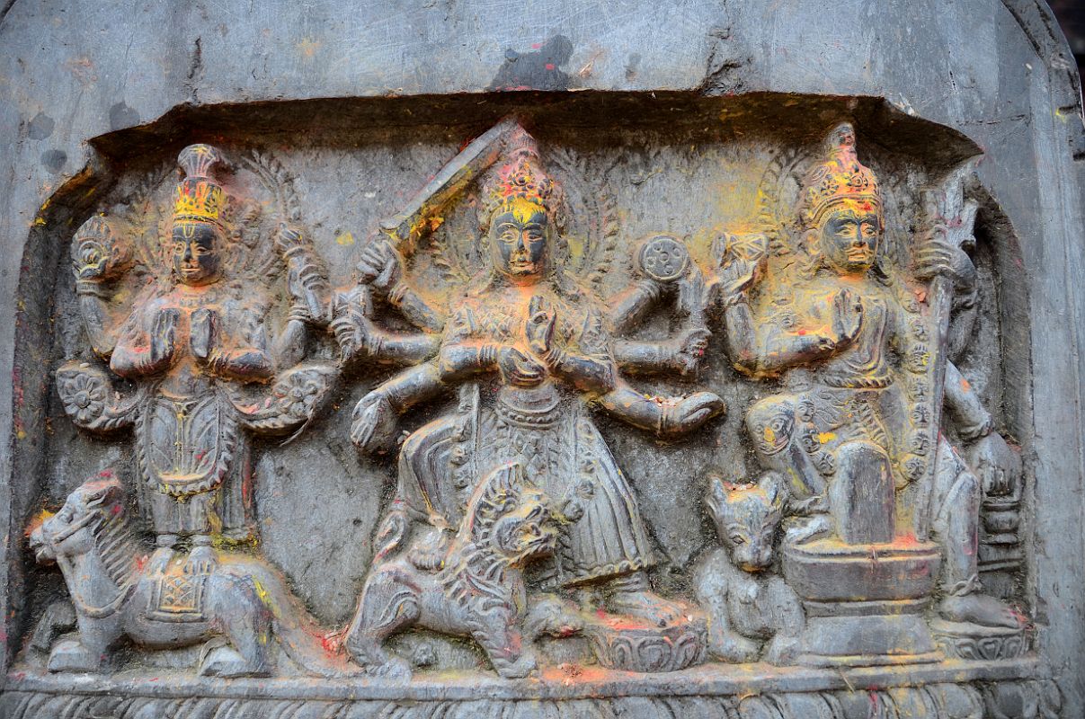 Kathmandu Changu Narayan 29 Vishnu, Durga, And Shiva Carvings On A Stone In Front Of The North Entrance To Changu Narayan Temple Vishnu, Durga, and Shiva are carved on a stone in front of the north entrance to Changu Narayan Temple. Vishnu has four arms and holds the disc and mace / club. Durga has eight arms and holds the sword, damaru drum, trident, and disc. Shiva has four arms and holds a damaru drum, a trident, and a small water pot.